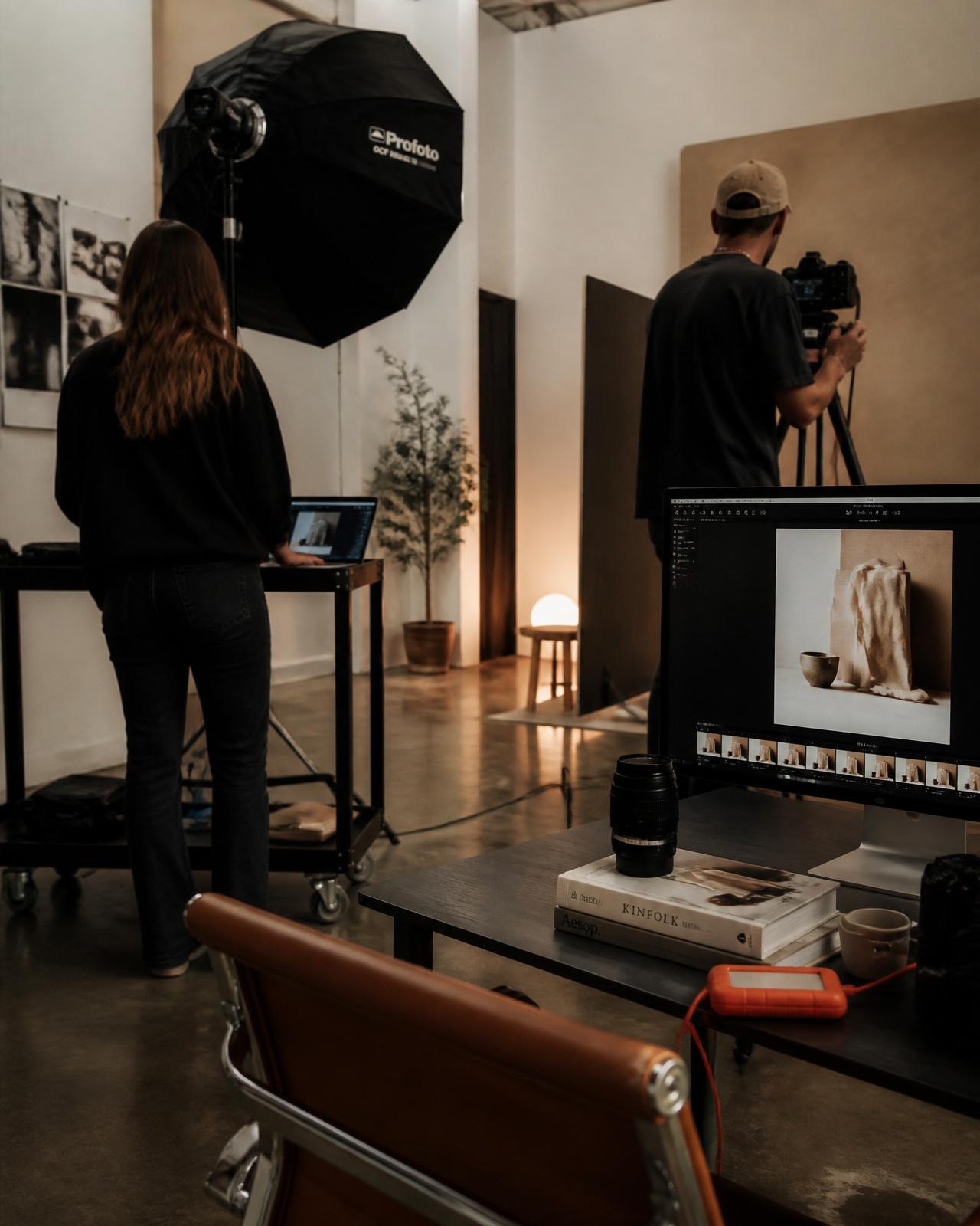 A photographer and videographer working with professional camera equipment and monitors inside a modern minimalist studio.